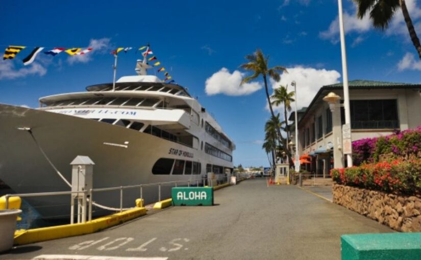 青空の下、ハワイ・ホノルルの港に停泊する大型クルーズ船「スターオブホノルル号」と、入り口に置かれたALOHAのサイン。