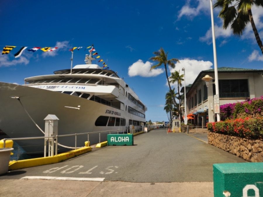 青空の下、ハワイ・ホノルルの港に停泊する大型クルーズ船「スターオブホノルル号」と、入り口に置かれたALOHAのサイン。