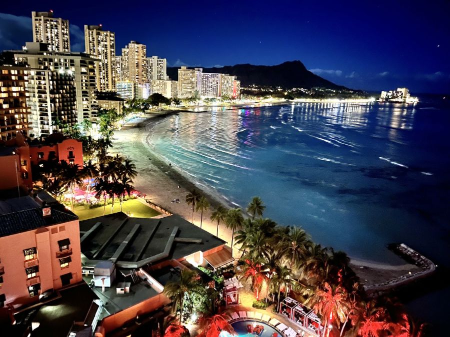 夜のワイキキビーチとダイヤモンドヘッドの全景。立ち並ぶホテルの明かりが海面に反射するホノルルの夜景。